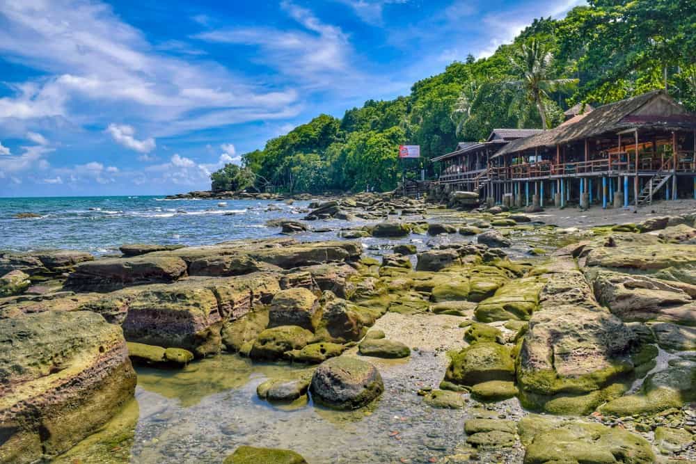 beach surrounded by moss covered stones and trees cambodia travel
