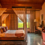 Four poster bed in a room with sofa, table, and an oversized window aahana resort ramnagar