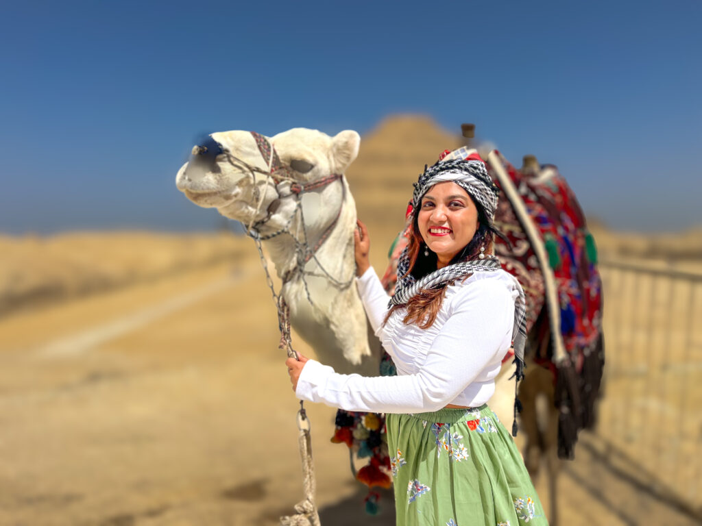 woman standing with a camel in front of a pyramid scams in egypt