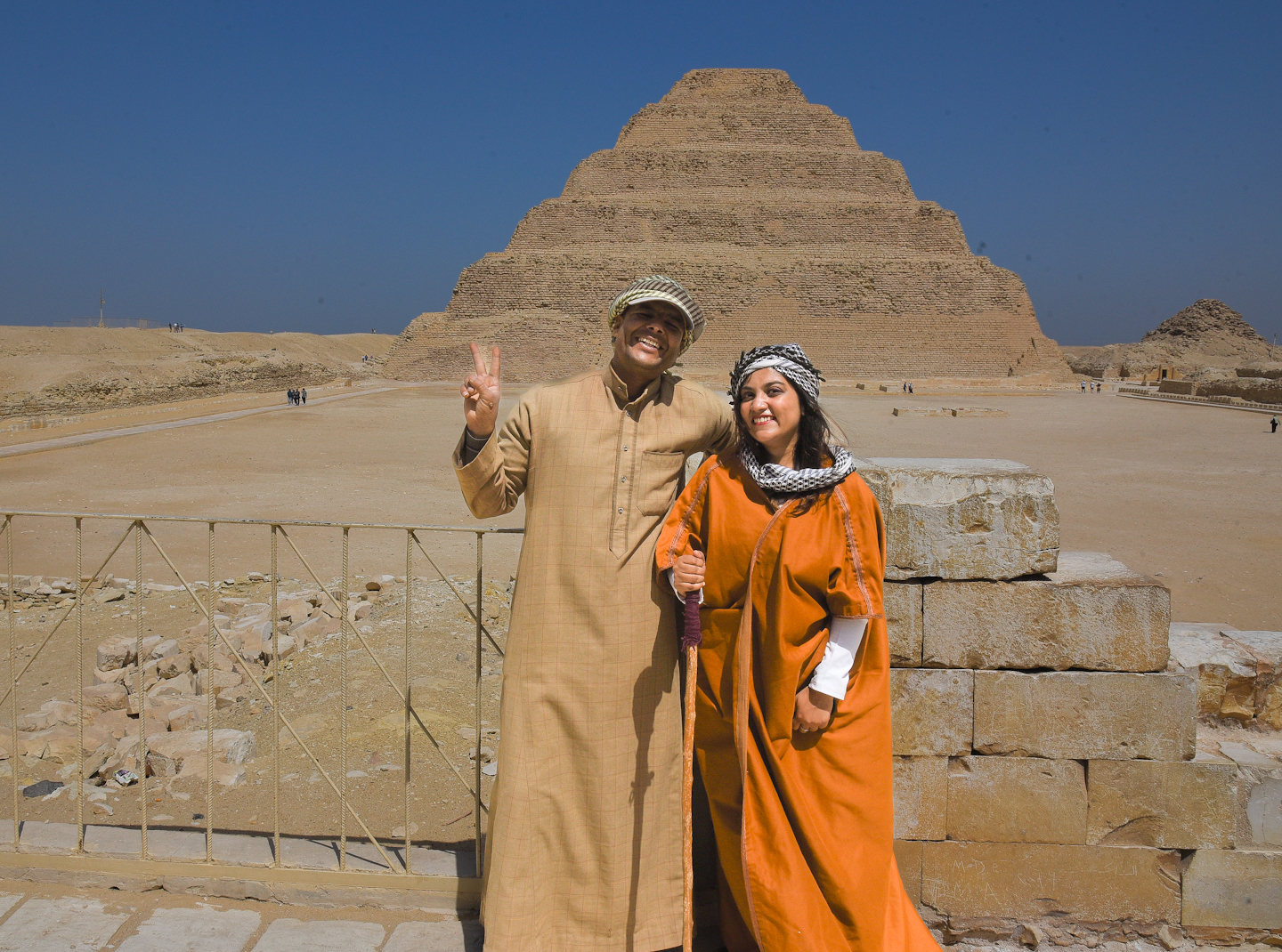 woman in orange standing with a man in front of a pyramid